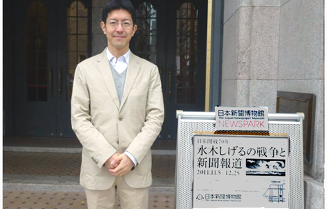 石坂わたるの活動:「水木しげるの戦争と新聞報道」の看板の前で。
